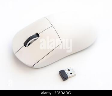 A white wireless computer mouse sits next to its USB receiver Stock Photo