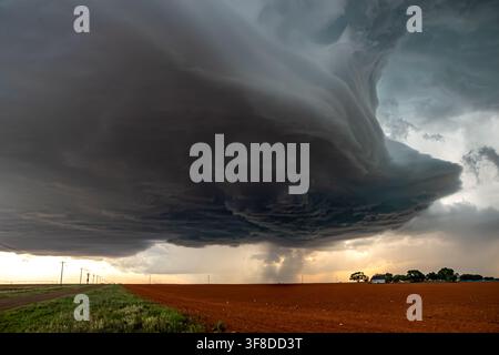 View of a massive supercell storm with dark swirling clouds and heavy rain over a vast agricultural field. Stock Photo