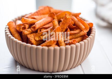 Close-up of spicy rolled corn chips in a ceramic bowl highlighting crunchy texture, vibrant red seasoning and savory flavor. a tasty snack perfect for Stock Photo