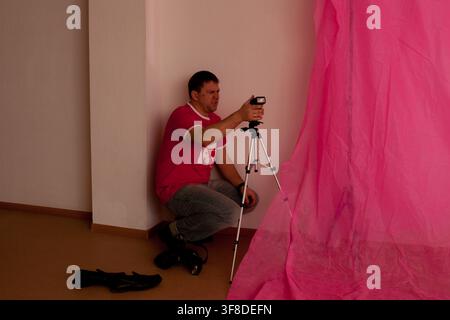 Moscow, Russia, 17.03.2012 Man photographer setting up his camera on a tripod next to a bright pink backdrop. Amateur photography or home studio conce Stock Photo