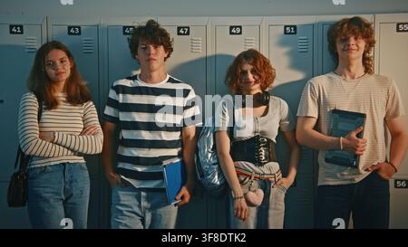 Teenage Standing Against School Lockers, Sharing Laugh and Talking, Wearing Casual Trendy Clothes and Holding School Supplies. School Life Socialization, Modern Youth Lifestyle on Campus. Portrait. Stock Photo