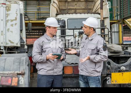 Two mechanics are discussing vehicle repairs using a tablet in a garage setting. Ideal for automotive maintenance, repairs, teamwork, and industrial w Stock Photo
