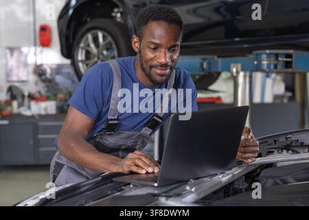 Car mechanic using a laptop to run diagnostic software for vehicle maintenance, modern computerised automotive repair. Stock Photo