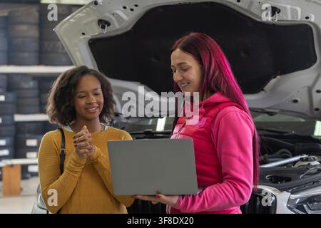 Female mechanic in a professional workshop in a positive interaction with a client, using a laptop to review a vehicle maintenance checklist. Stock Photo