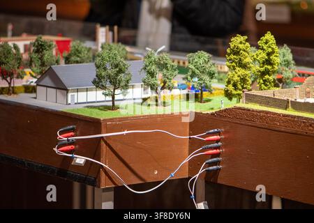 A close view shows a tabletop miniature scene with small buildings, trees, grass, and electrical wires connected across wooden sections. Stock Photo