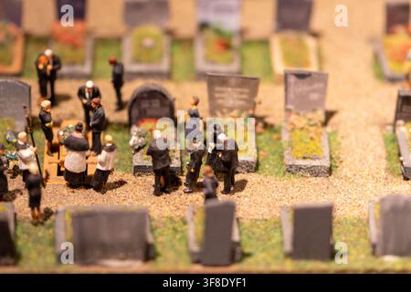 A close-up view shows tiny figurines attending a funeral among gravestones in a cemetery diorama. Stock Photo