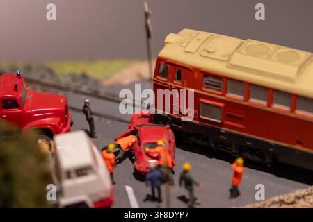 A close-up photograph shows a miniature railway accident diorama with a red locomotive, a crushed red car, emergency vehicles, and small figures on a Stock Photo