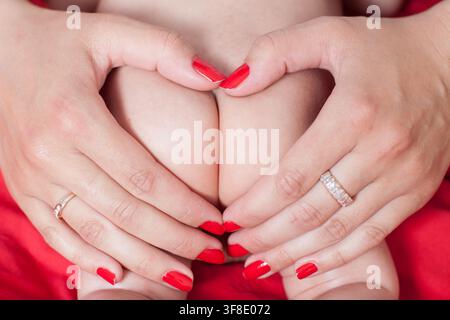 A mother forms a heart shape with her hands around her baby's adorable bottom. Stock Photo