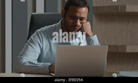 Tired Indian Arabian business man yawning in office bored with computer laptop work evening deadline exhausted businessman manager fatigued no energy Stock Photo
