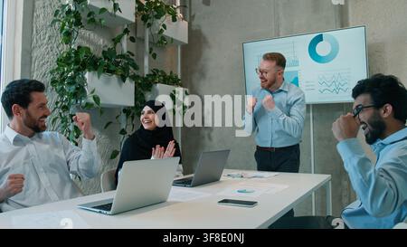 Cheering happy diverse multiethnic business team celebrating success startup indoor office Arabian businessmen muslim businesswoman victory work Stock Photo