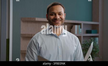 Joyful Indian Arabian business man smiling looking camera indoor office laptop workplace happy American businessman entrepreneur employer manager Stock Photo