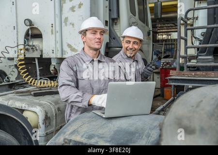 Two mechanics working together on a laptop in an auto repair shop to enhance workflow efficiency. Ideal for automotive, teamwork, and technology-relat Stock Photo