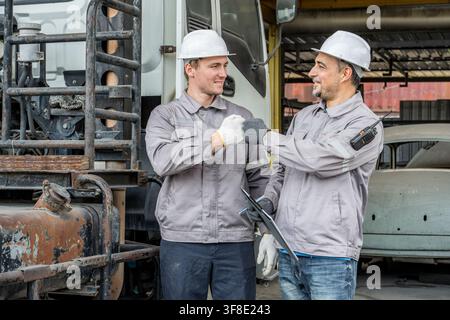 Two male workers celebrating success with a fist bump in an industrial garage, symbolizing teamwork and motivation. Ideal for business, teamwork, and Stock Photo