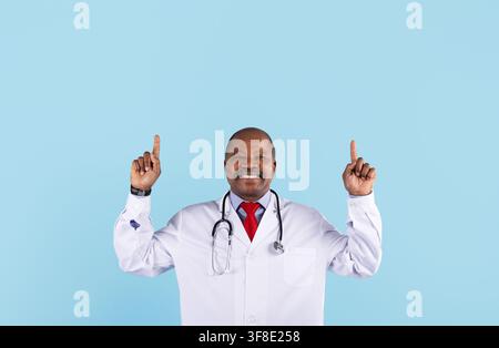 Smiling mature African American doctor pointing upward with both hands Stock Photo