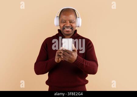 Smiling mature African American man wearing wireless headphones while using smartphone Stock Photo