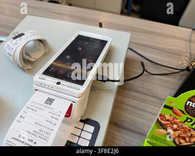 Minsk, Belarus - August 04, 2026: Mobile payment device with printed receipt on counter, snack packaging and paper rolls visible in retail environment Stock Photo