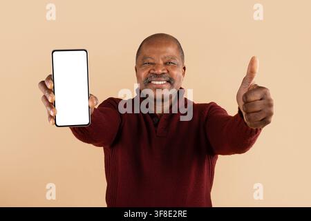 Happy mature African American man showing blank smartphone and giving thumbs up Stock Photo