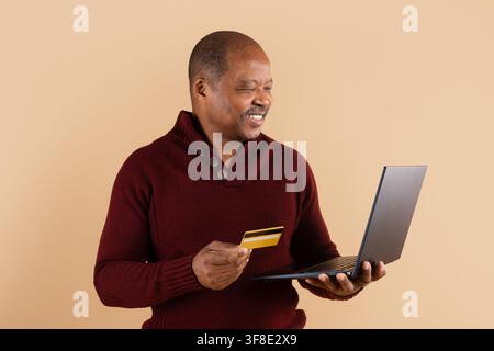 Mature African American man holding credit card while using laptop Stock Photo