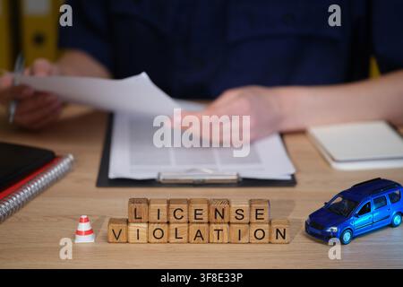 License violation notice on a busy desk with paperwork and a miniature car during a professional meeting Stock Photo