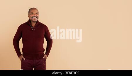 Cheerful black man in burgundy sweater looking away with hands in pockets Stock Photo
