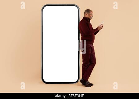 Mature African American man using smartphone beside large blank mobile mockup Stock Photo
