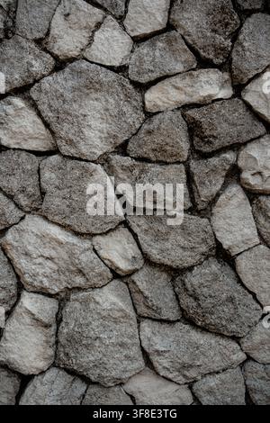 Stone wall texture featuring irregular grey rocks in vertical composition. Stock Photo