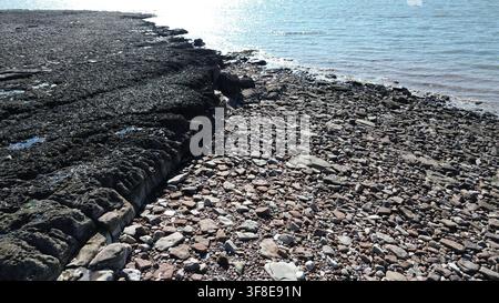 Aerial detail of layered rock ledges and shingle on a Welsh wave-cut platform at low tide Stock Photo