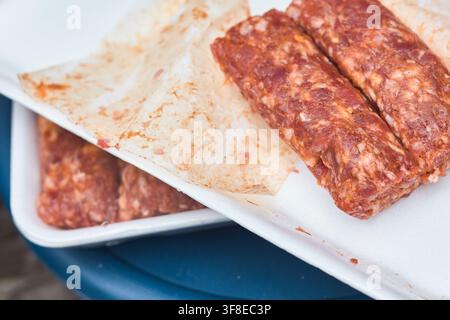 Raw traditional Romanian mici skinless minced meat rolls arranged on a white tray ready for grilling. Romania. Stock Photo