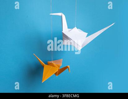 White and Orange Origami Paper Cranes Hanging Against Bright Blue Background Stock Photo
