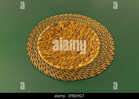 Round woven wicker placemat with braided seagrass texture on solid green background, top-down view Stock Photo