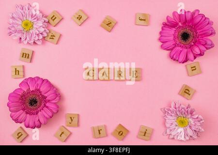 Flat lay view of wooden letters spelling word CARE surrounded by pink gerbera and chrysanthemum flowers on pink background self care beauty concept st Stock Photo