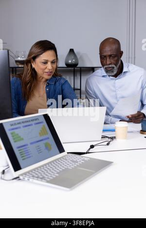 Two mature African American colleagues reviewing silver laptop sales chart at table in dress shirts Stock Photo