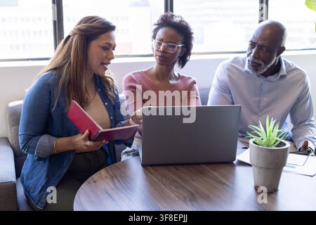 African American colleagues sitting around round wooden table in office lounge using silver laptop. Coworkers, collaboration, teamwork, meeting, discu Stock Photo