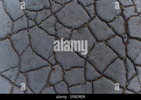 Cracked dark asphalt road texture, showing deep fissures and weathered surface patterns for industrial design backdrops, urban decay and weathered ground background Stock Photo
