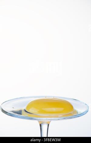 Close up of a large egg yolk on a glass coupe stand, bright white background Stock Photo