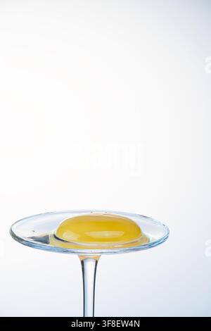Whole egg yolk on a glass coupe stand against a cool white background, food photography Stock Photo
