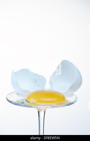 Egg yolk on a glass coupe with cracked shell opened wide on both sides, bright background Stock Photo