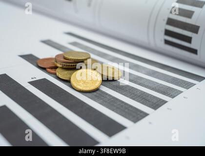 During a business analysis session, coins are placed on printed charts that show financial data. The charts feature bar graphs and numerical figures. Stock Photo