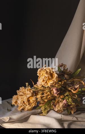 Loose bouquet of dried roses resting on white fabric, warm side light still life Stock Photo