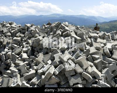 View of a large pile of grey concrete paving blocks stacked outdoors with rolling mountains in the background in Posof, Ardahan, Turkiye. Stock Photo