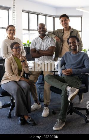 Diverse coworkers in business clothes smiling sitting on chairs in office by windows with backpack. Team, professionals, teamwork, daylight, workspace Stock Photo
