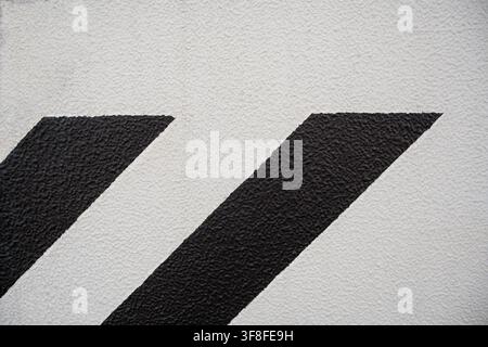 Black diagonal stripes painted on a white textured concrete wall background. Stock Photo