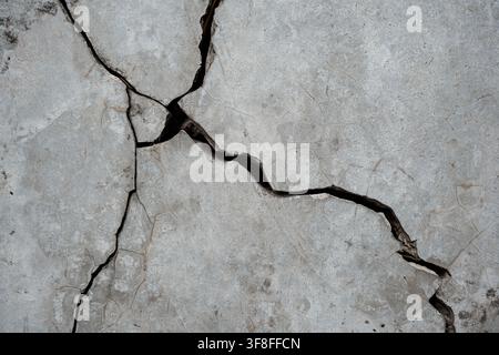 Cracked concrete surface texture with deep fissures and weathered gray cement structure. Stock Photo
