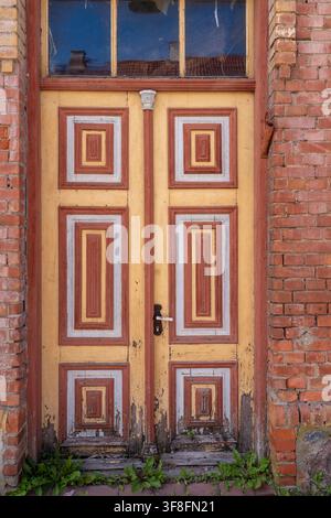 Weathered old wooden double door with peeling yellow and red paint, decorative geometric panels and aged brick walls. Stock Photo