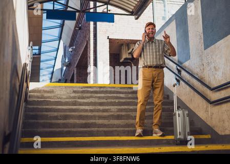 Senior man is standing at railway station and talking on mobile phone. Senior people traveling. Stock Photo