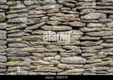 Weathered traditional stone wall with irregular layered rocks and natural lichen creating a rustic architectural texture. Stock Photo