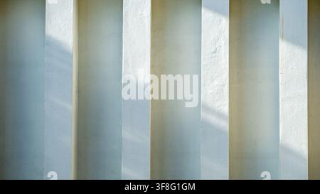 White concrete pillars wall with minimalist architecture pattern, natural sunlight shadow lines on cement surface, modern building texture background, Stock Photo