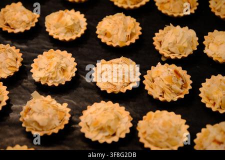 High-angle view of mini almond tarts topped with sliced almonds arranged on a black background. Stock Photo