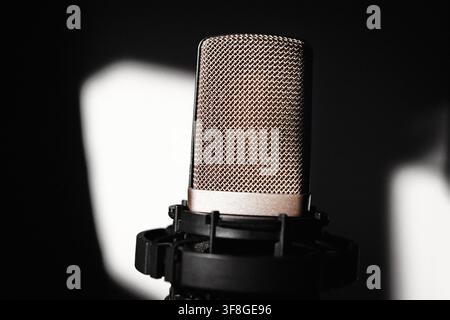 Studio microphone with large diamond mesh pop filter grille, lit against black background with soft light patches behind. Shock mount cradles Stock Photo
