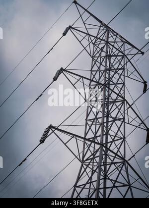 Low angle view of a tall metal electrical transmission tower with high voltage power lines against a cloudy sky Stock Photo
